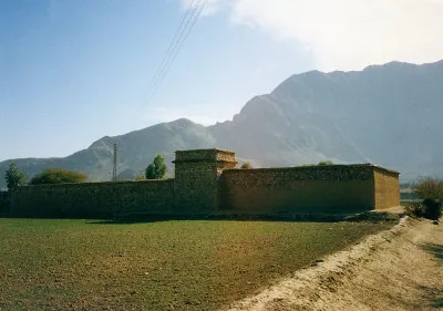 A walled, fortress-like family compound with a watchtower beneath bare mountains